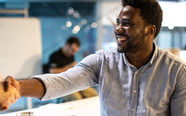 Man in office shakes hand of colleague and smiles