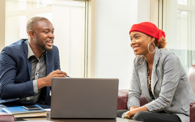 Male and female colleague smile in an office environment as they discuss work 