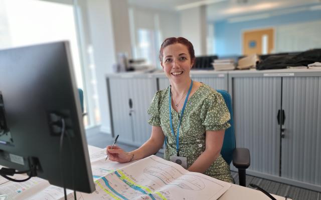 White female smiles at the camera. She is working at a desk in a Leeds City Council office.