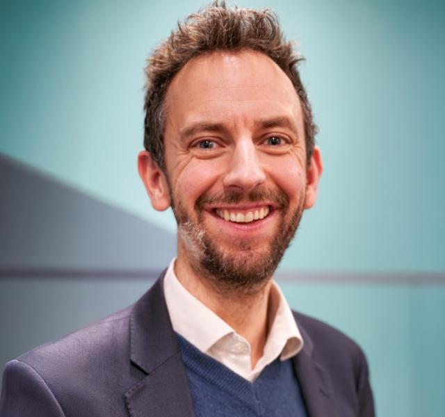 Image shows Chief Executive Ed Whiting smiling at the camera wearing a blue jumper and blazer
