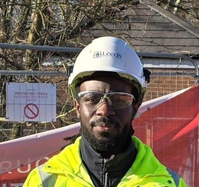 A male engineer wears a hard hat, safety glasses and high visibility clothing on a building site for new houses.
