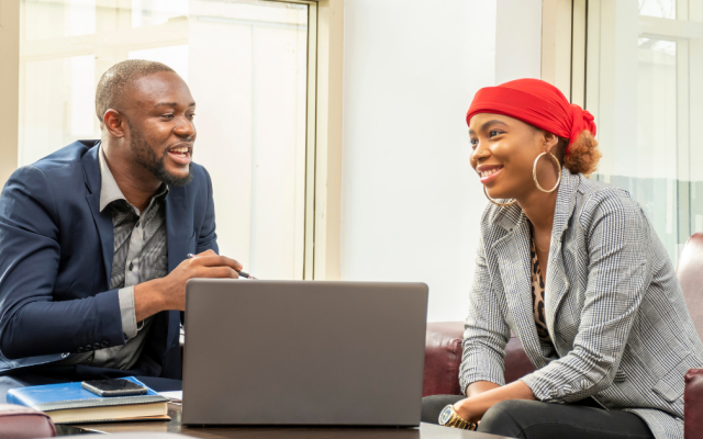 Male and female colleague smile in an office environment as they discuss work